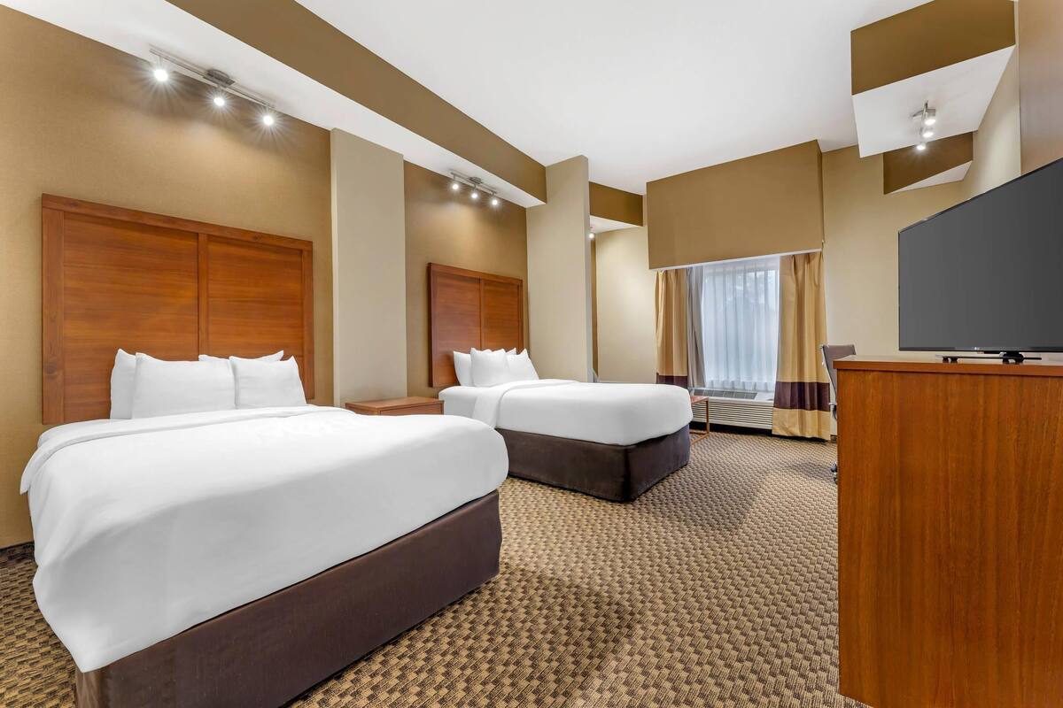 A hotel room with two beds, a TV, and a desk.