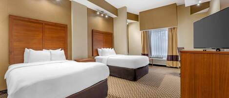 A hotel room with two beds, a TV, and a desk.