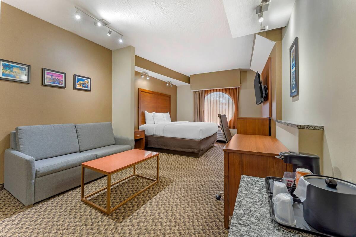 A hotel room with a bed, a sofa, a small table, a desk, and a coffee maker.
