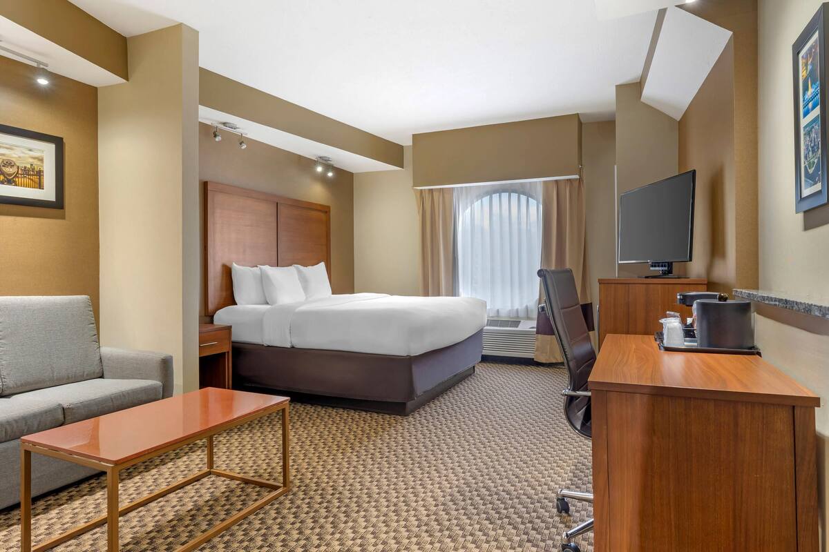A hotel room with a bed, a desk, a chair, a sofa, and a television.