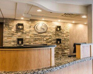 Zona de recepción con pared de piedra, un gran logotipo en forma de S y un mostrador de madera.