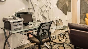 A modern office space with a glass desk, a printer, a computer, a black office chair, a glass table, and a stone accent wall.
