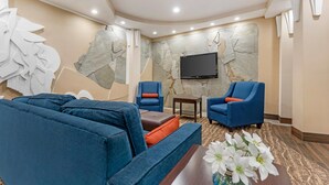 Una sala de estar moderna con un sofá modular, dos sillones, una mesa de centro y un televisor de pantalla plana montado en una pared de piedra.
