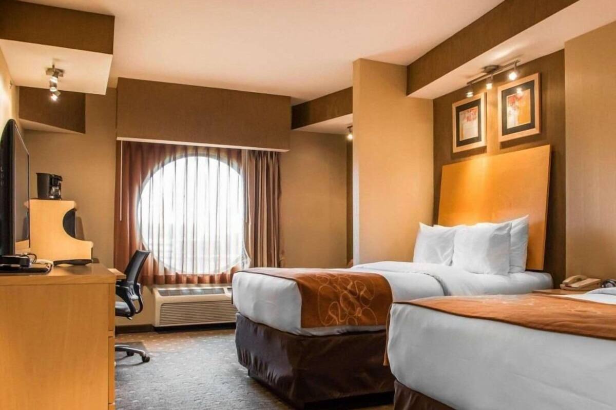 A hotel room with two beds, a desk, a chair, a coffee maker, and a large window with curtains.