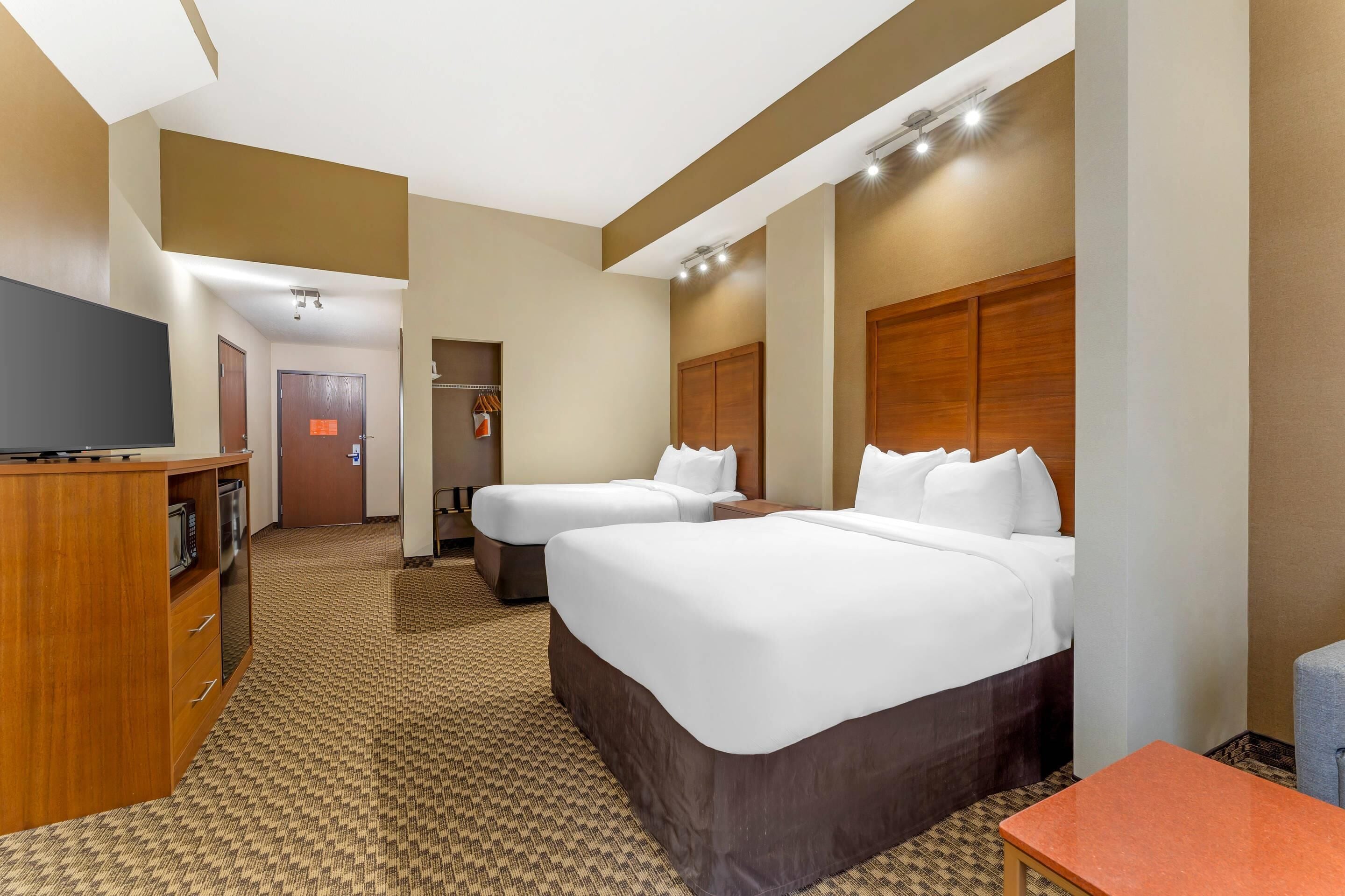 A hotel room with two beds, a TV, a desk, and a carpeted floor.
