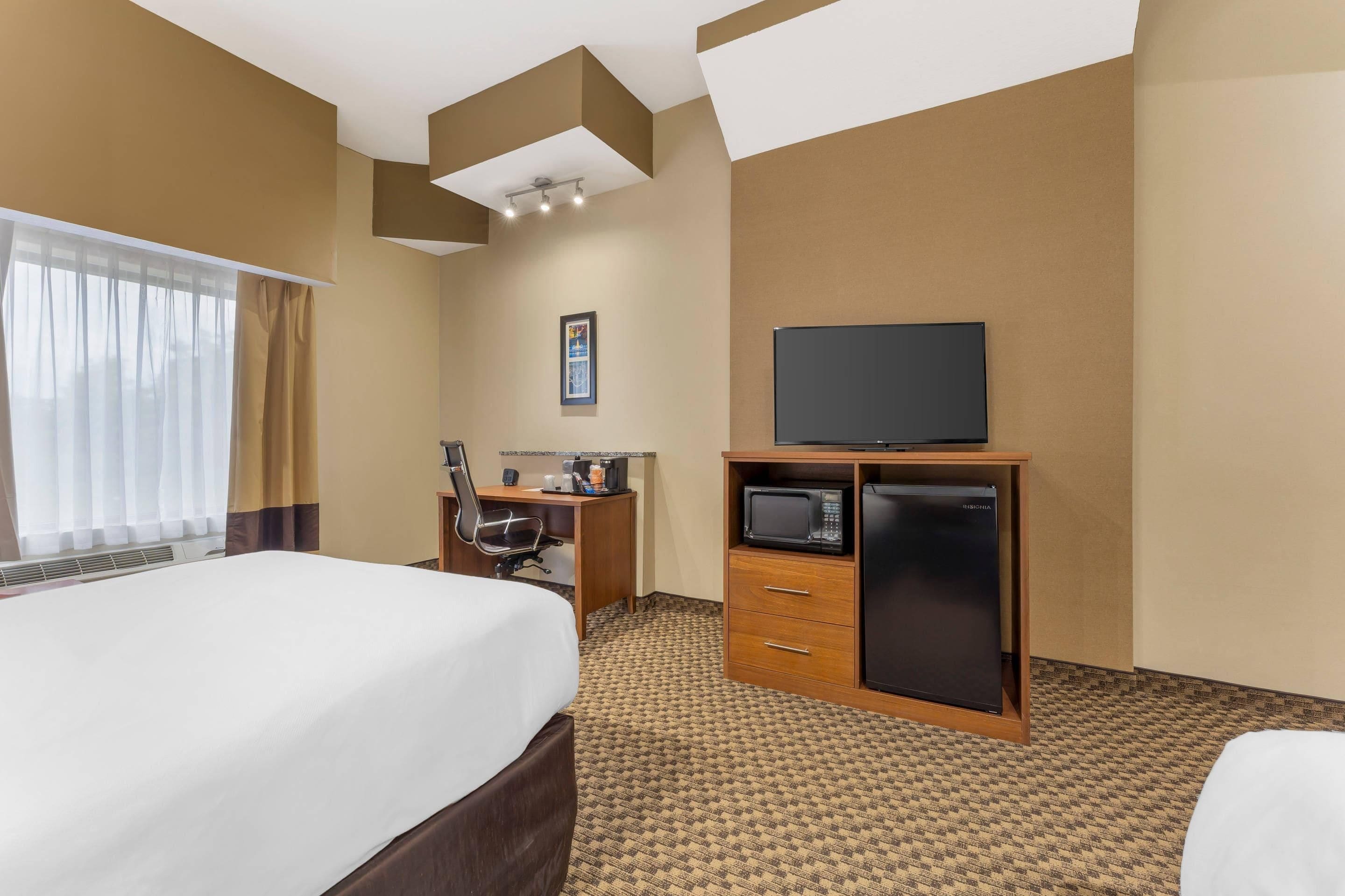 A hotel room with a bed, a desk with a chair, a television, a refrigerator, and a microwave.