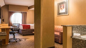 Habitación de hotel con cama, escritorio, silla, sofá y baño con encimera de granito.