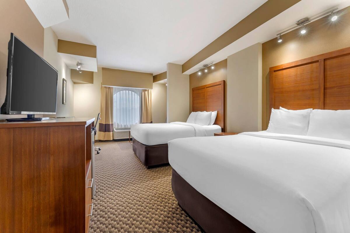 A hotel room with two beds, a TV, and a desk.