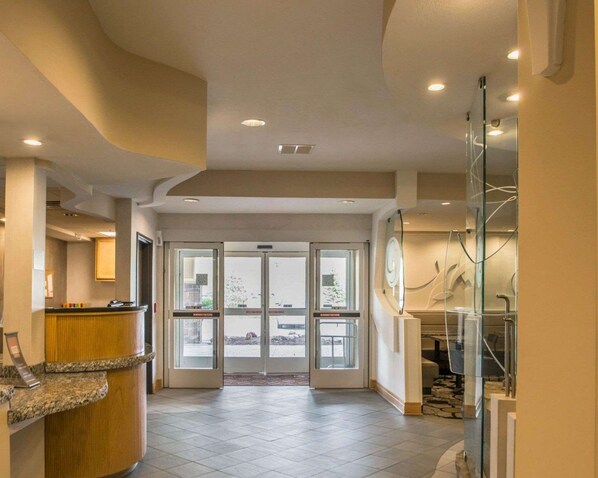 A hotel lobby with a reception desk, a glass wall with a view, and a tiled floor. - Comfort Suites Monroeville - Pittsburgh East (Monroeville)