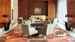 A lobby with a round table surrounded by chairs, a sofa, and a painting on the wall. - Le Meridien Towers Makkah (Makkah)