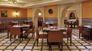 A restaurant with checkered flooring, patterned walls, and red patterned chairs. Tables are set with white tablecloths and silverware. - Le Meridien Towers Makkah (Makkah)