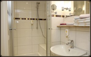 Un baño con ducha de vidrio, un lavamanos con espejo y un perchero con toallas dobladas.