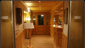 A wooden interior with a central hallway leading to a door, flanked by wooden cabinets and a small table with a menu stand. - Parkhotel Waldlust (Häusern)