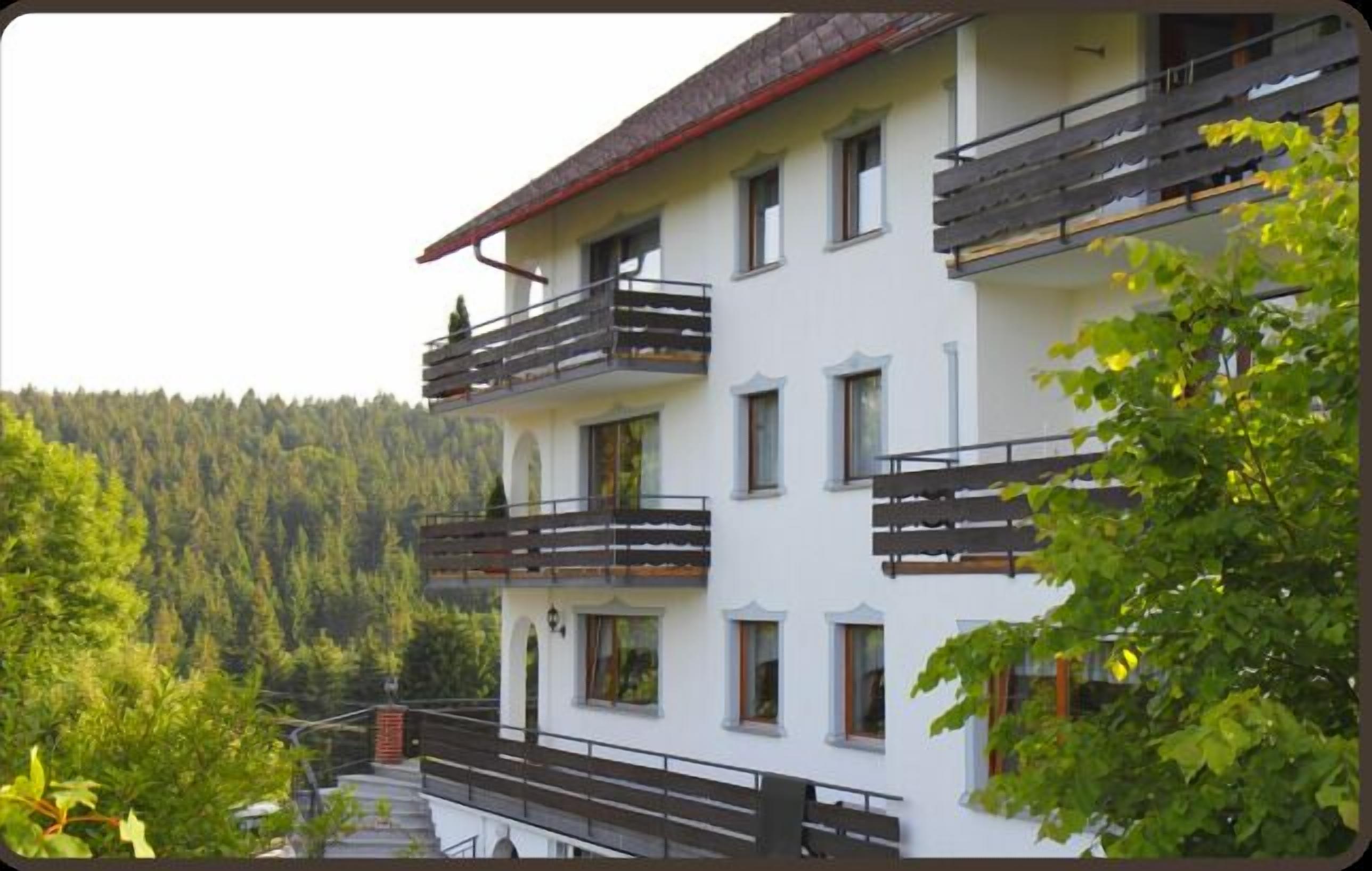 Un edifici de diverses plantes amb balcons, envoltat per una zona boscosa.
