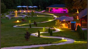 A well-lit outdoor area with pathways, seating under umbrellas, and a building with a roof. - Parkhotel Waldlust (Häusern)