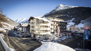 A multi-story hotel with balconies, a ski resort sign, and a mountain backdrop. - Hotel Valentin (Soelden)