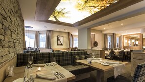 A restaurant with a stone wall, wooden ceiling, and a ceiling light. Tables are set with plates, cutlery, and glasses. - Hotel Valentin (Soelden)