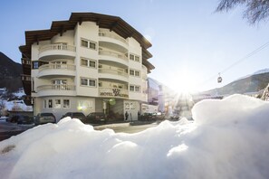 Ett hotell med flera våningar, balkonger, en skylt som visar att det finns skidåkning i närheten och utsikt över bergen.