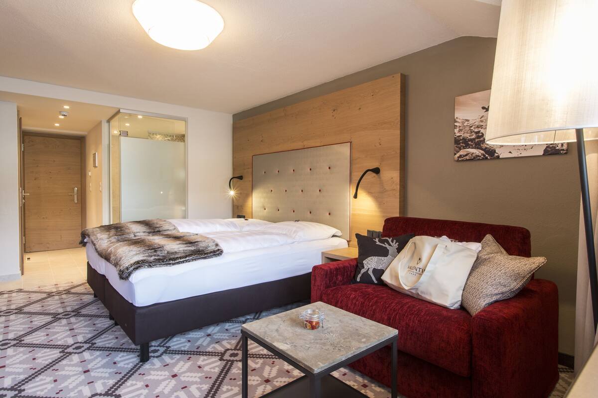 Une chambre d’hôtel avec un grand lit, un canapé rouge, une petite table et une lampe fixée au mur.