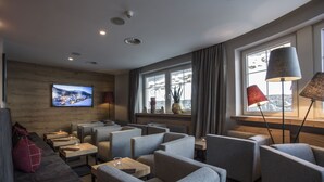 A modern interior with seating areas, a large window with a view, and a flat-screen TV on the wall. - Hotel Valentin (Soelden)