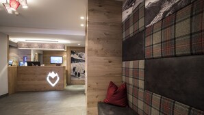 A reception area with a wooden desk, a heart-shaped logo, a television, and a couch with plaid cushions. - Hotel Valentin (Soelden)