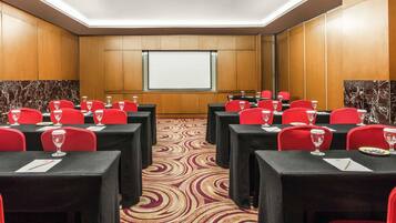 A conference room with tables, chairs, a projector screen, and a patterned carpet.