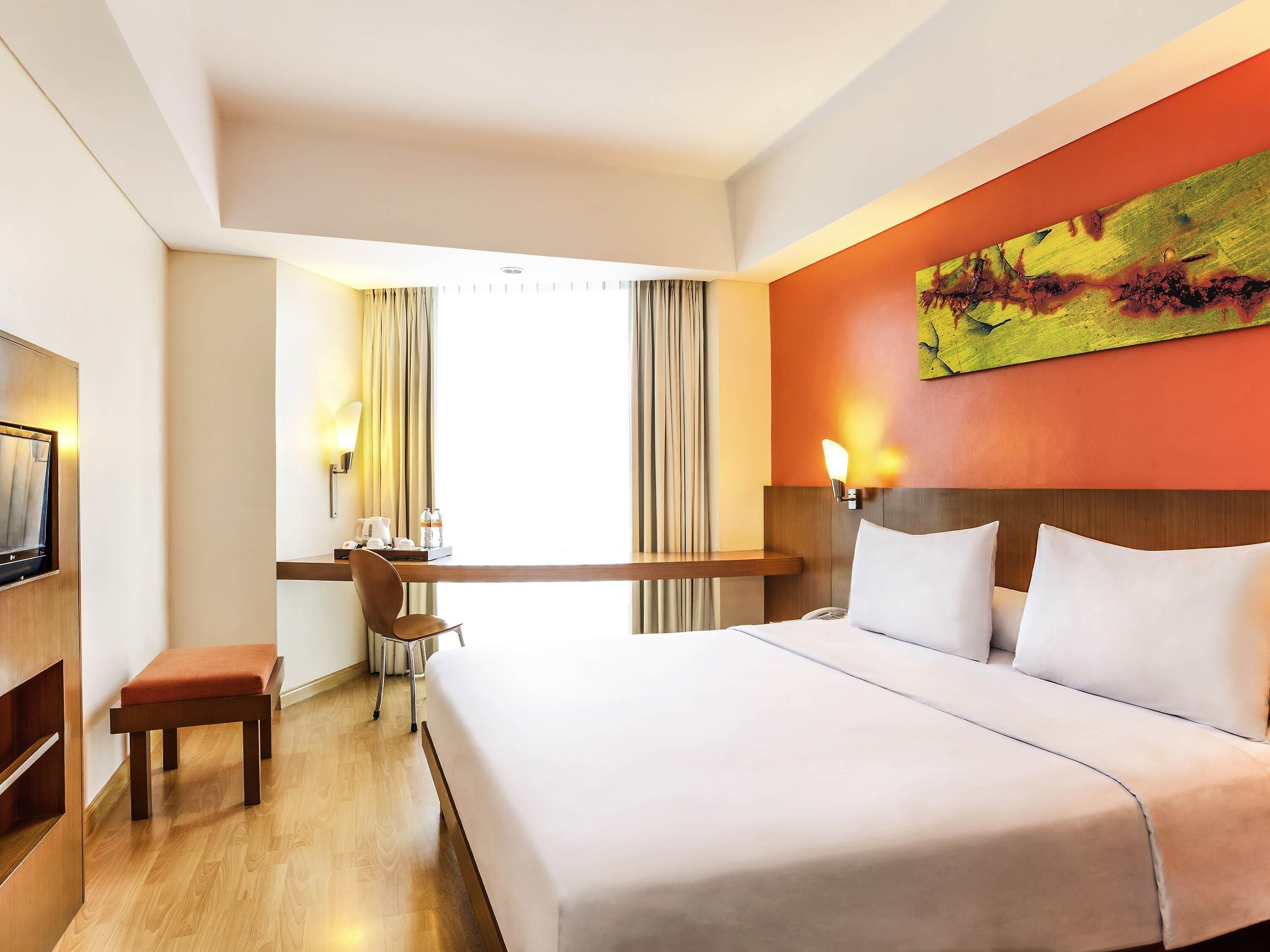 A hotel room with a bed, a desk, a chair, and a painting on the wall.