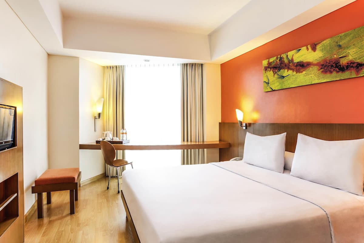 A hotel room with a bed, a desk, a chair, and a painting on the wall.