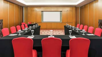 Un salón de conferencias con una larga mesa, sillas rojas y una pizarra.