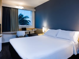 Habitación de hotel con una cama grande, un escritorio con una computadora portátil, una silla y una ventana con cortinas.
