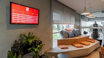 Un interior moderno con una gran pantalla digital que muestra información de vuelos, una zona de estar con cojines y plantas en macetas.