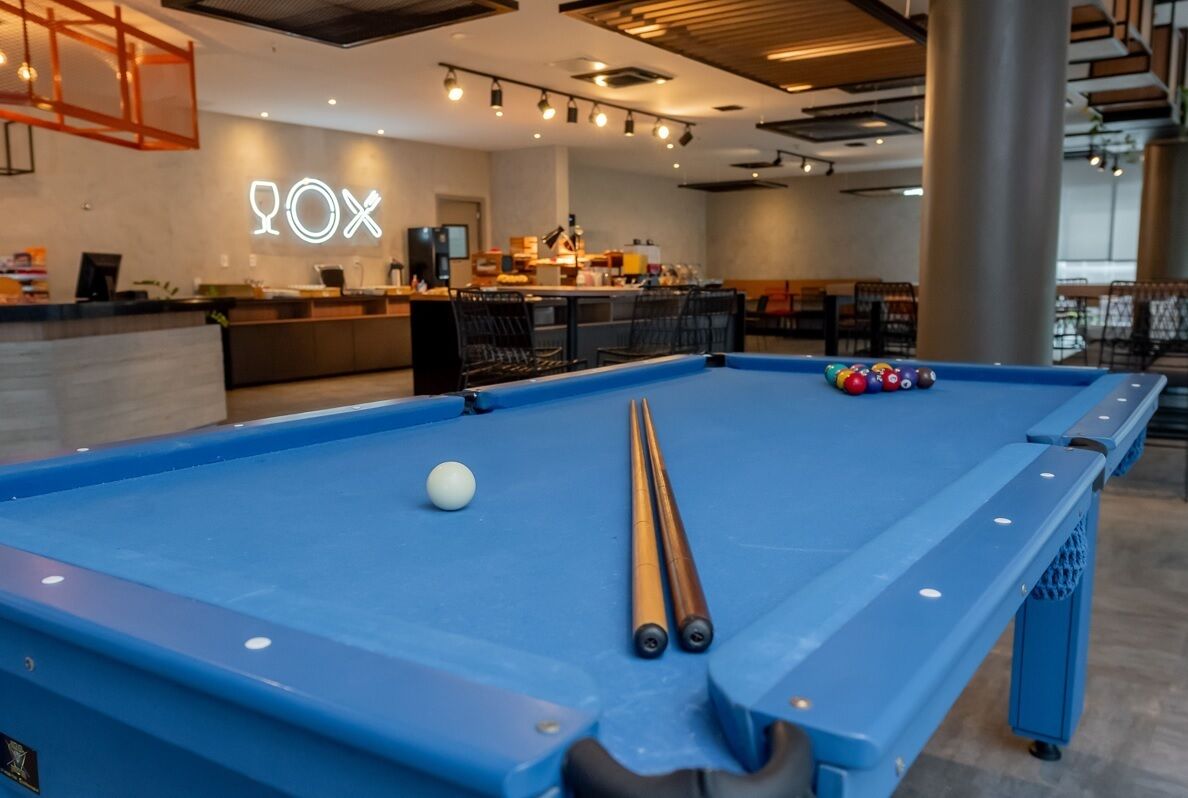 Una mesa de billar con bolas y tacos, un mostrador de recepción y una zona de bar en un espacio interior moderno.