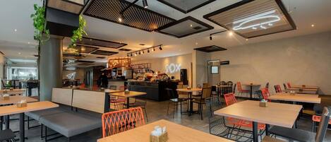 Un interno di un caffè moderno con diverse zone di seduta, un bancone e una cucina visibile sullo sfondo.