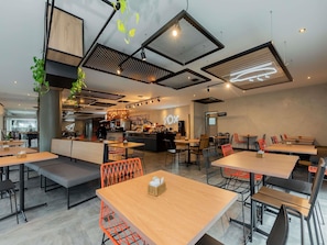 Un café moderno con varias zonas de estar, una barra y una cocina visible al fondo.