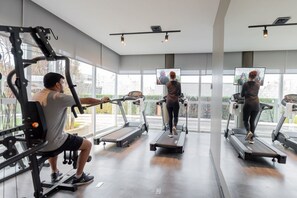 Een sportschool met loopbanden, krachtapparaten en een grote spiegel.