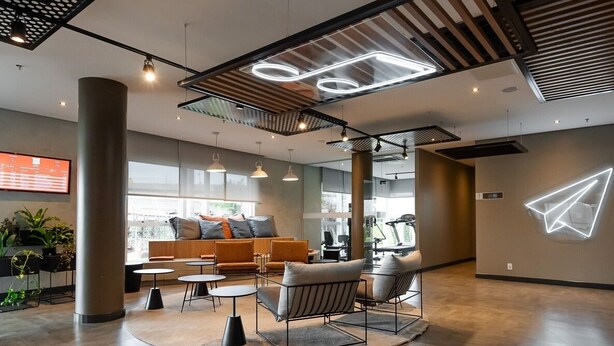 A modern lounge area with seating, a large pillar, and a visible gym in the background.