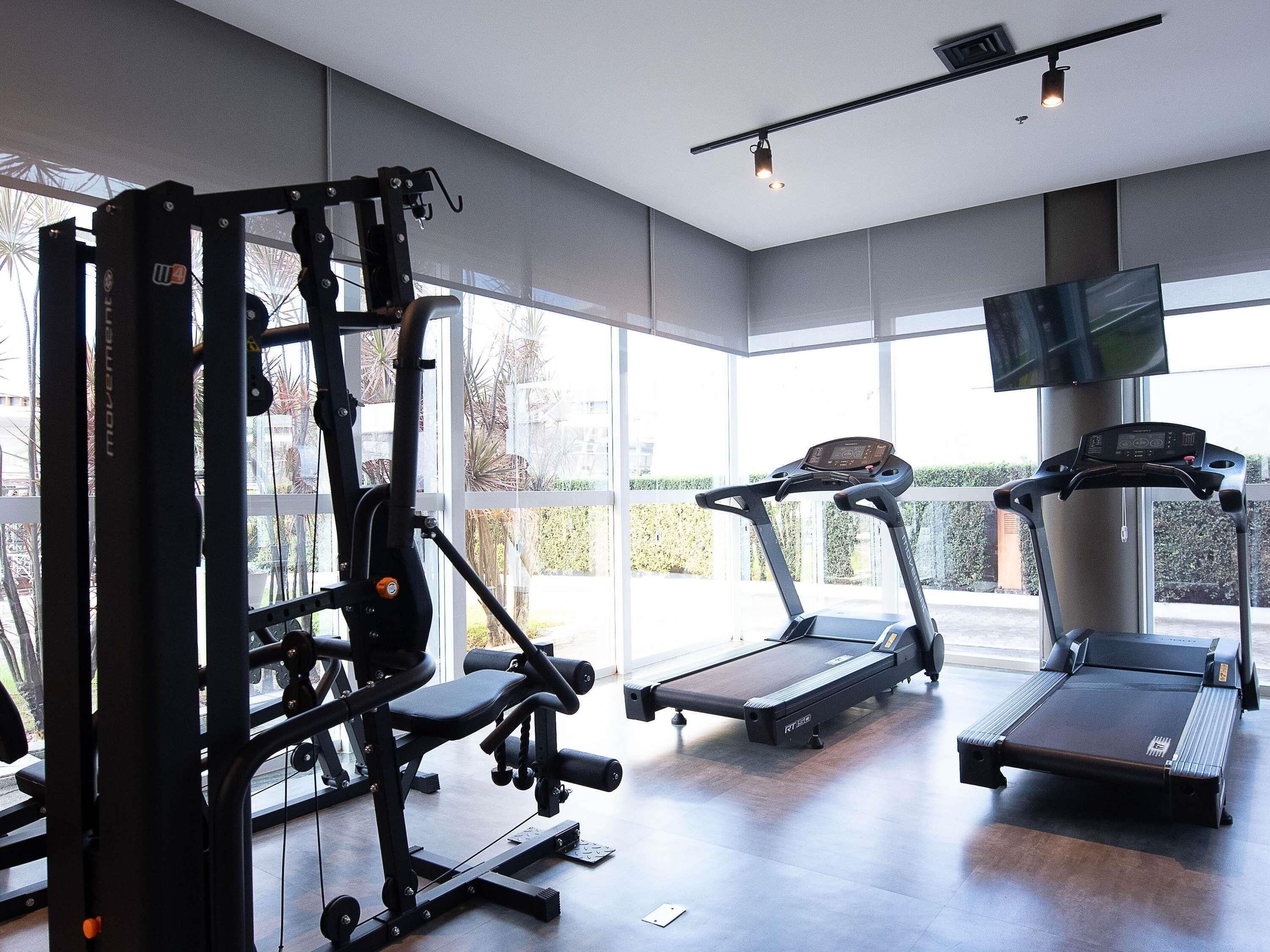 A gym with cardio machines, weightlifting equipment, and large windows.