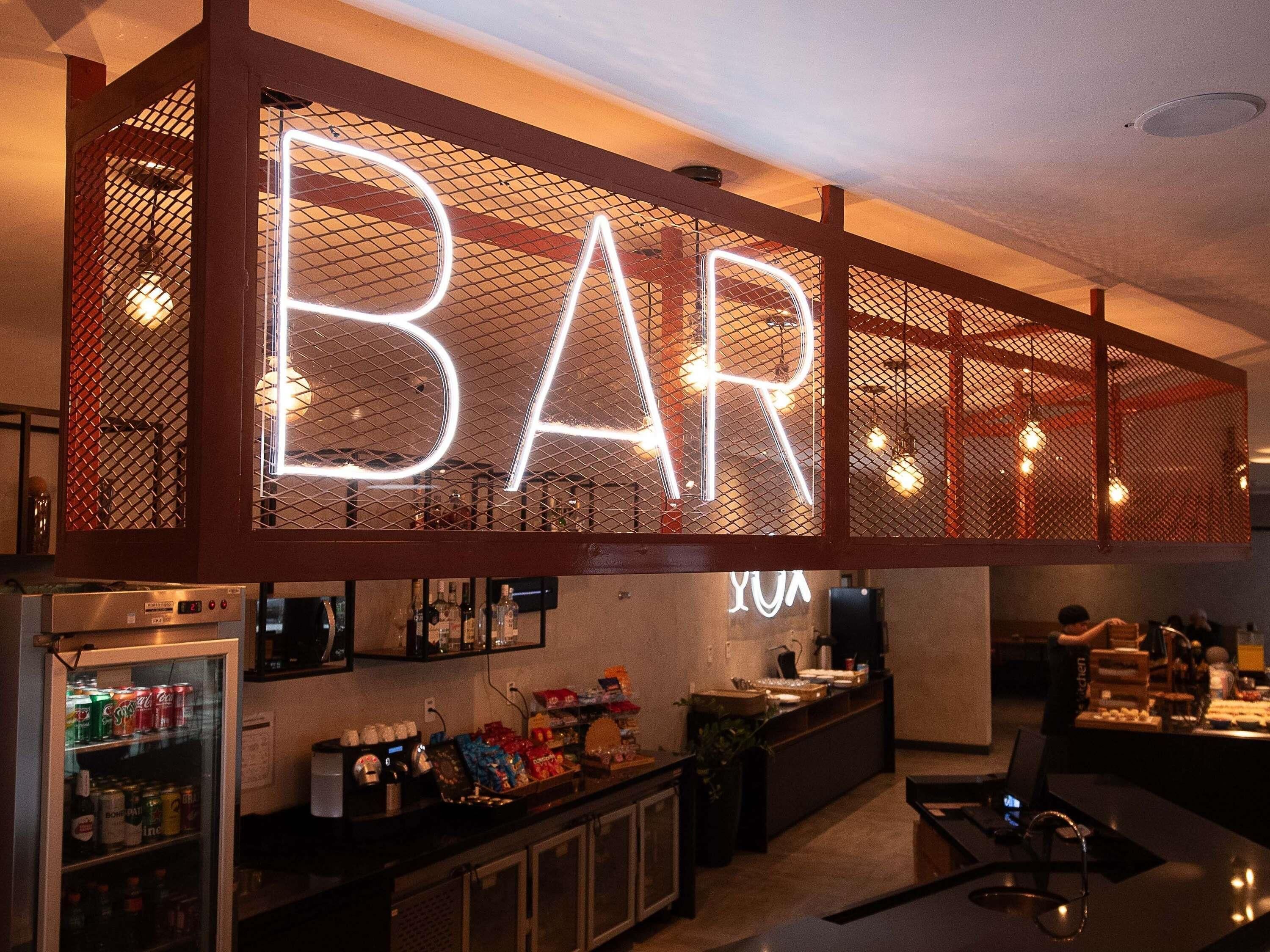 Zona de bar con un letrero de neón que dice 'BAR' y una barra con distintos objetos.