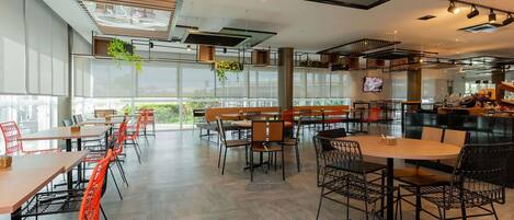 A modern cafe interior with high ceilings, large windows, and a variety of seating arrangements including tables and chairs.