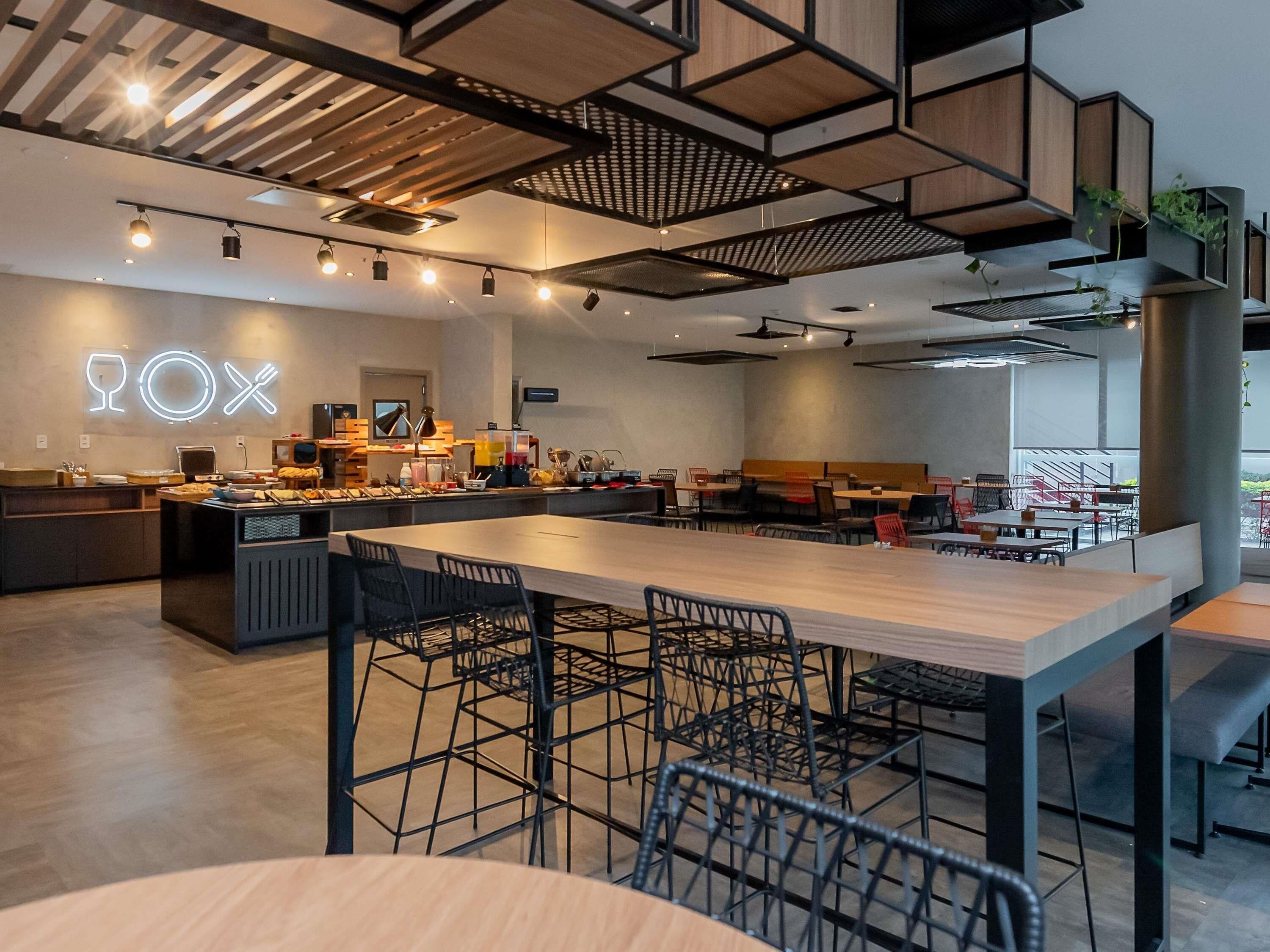 A modern restaurant interior with a central dining area, bar seating, and a neon sign.