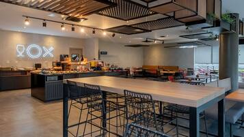 A modern restaurant interior with a central dining area, bar seating, and a neon sign.