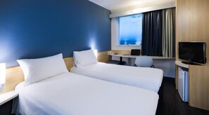 A hotel room with two beds, a desk with a laptop, a television, and a window with curtains. - ibis Vitoria Aeroporto (Serra)