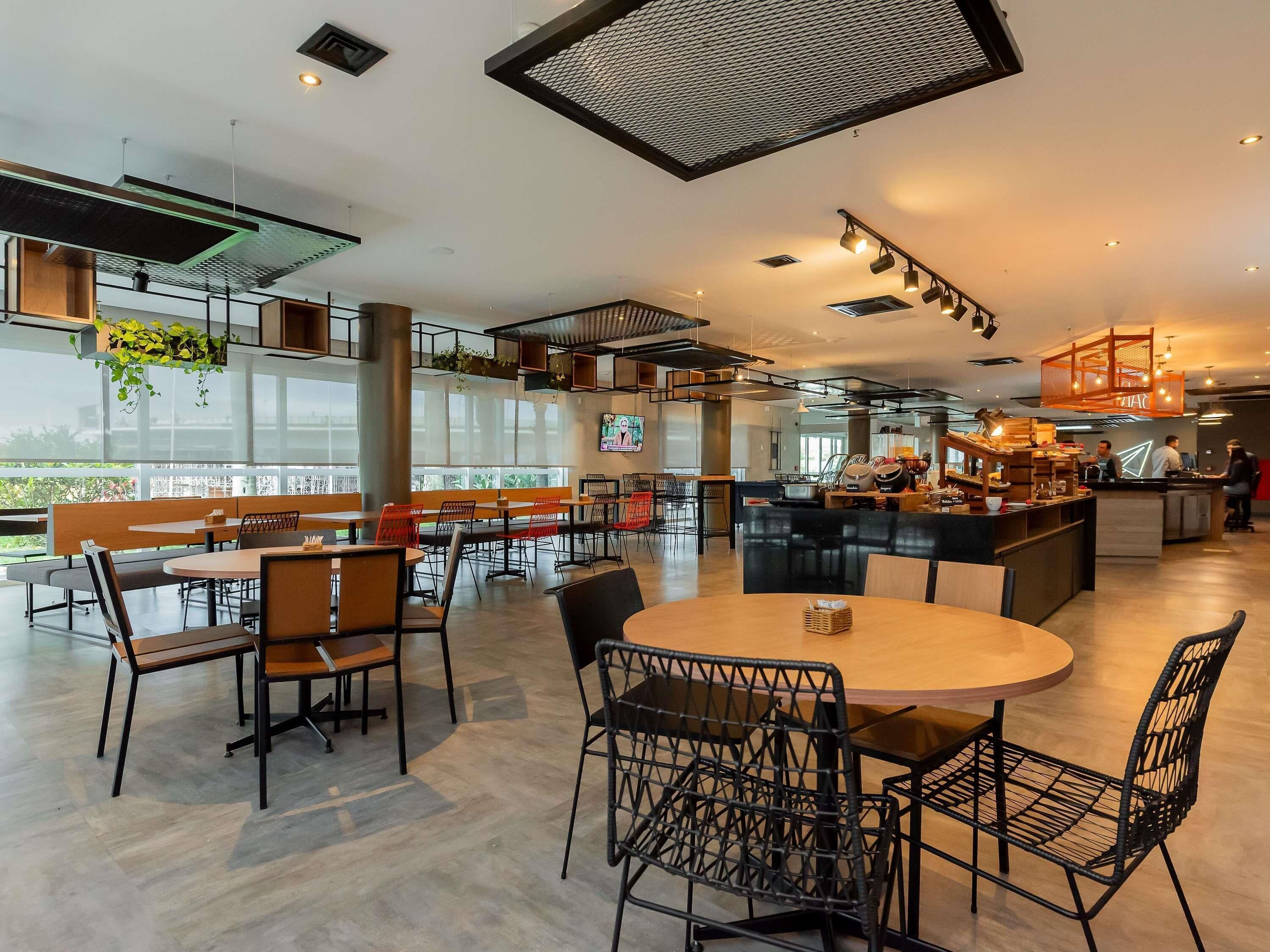 Un café moderno con mesas y sillas altas, una zona de bar y amplios ventanales con vistas.