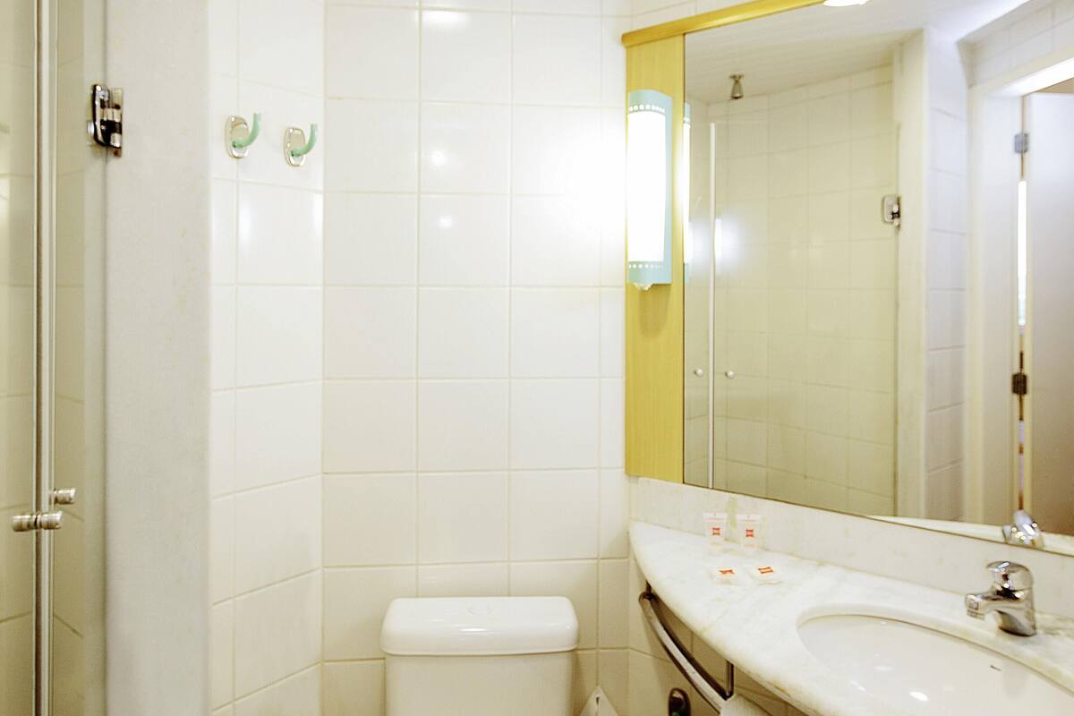 A bathroom with white tiles, a toilet, a sink with a mirror, and a shower area.