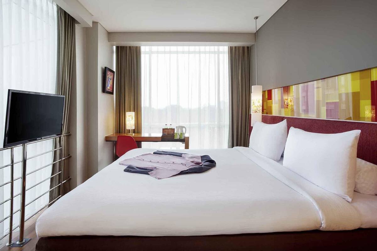 A hotel room with a bed, a TV, a desk, and a view of the city.