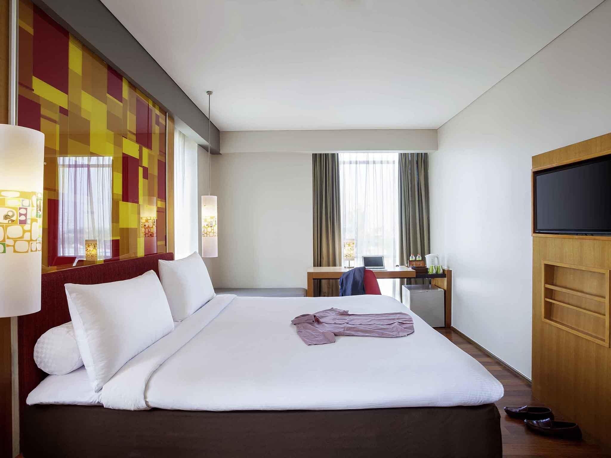A hotel room with a large bed, a desk with a laptop, a television, and a window with curtains.