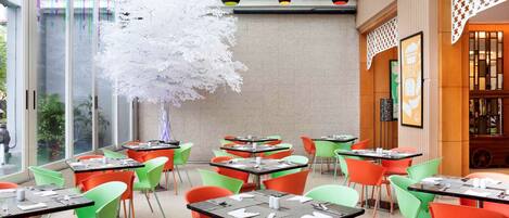 A restaurant with colorful chairs and tables, a decorative tree, and a lattice ceiling.