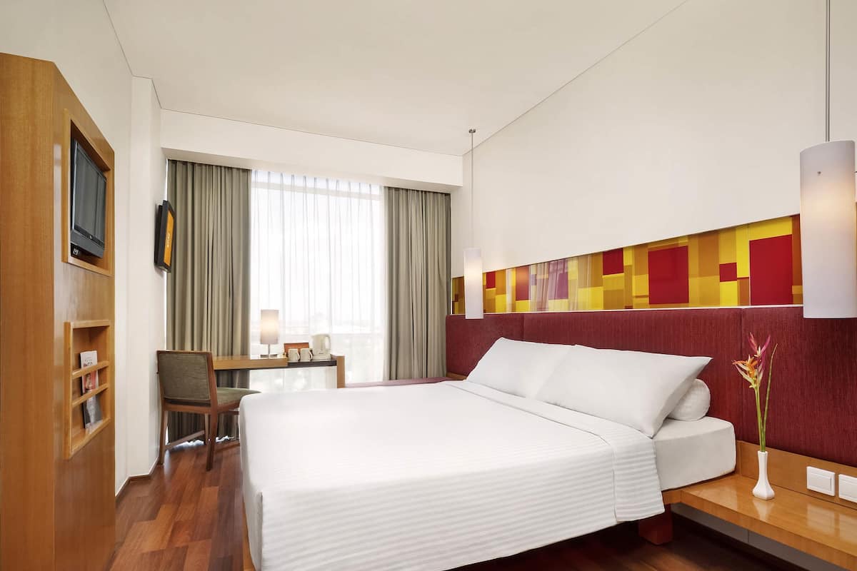 A hotel room with a large bed, a desk with a chair, a TV, and a window with curtains.