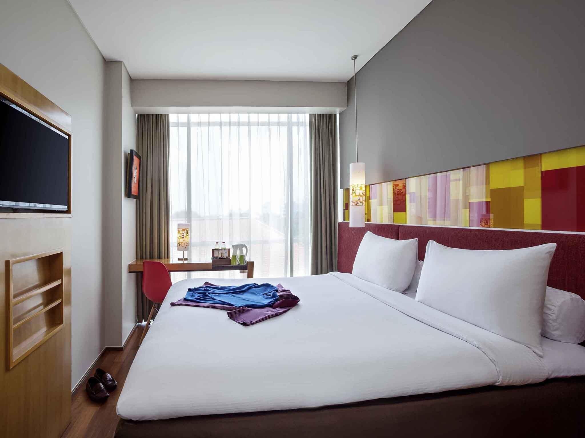A hotel room with a large bed, a desk with a chair, a TV, and a view of the city.
