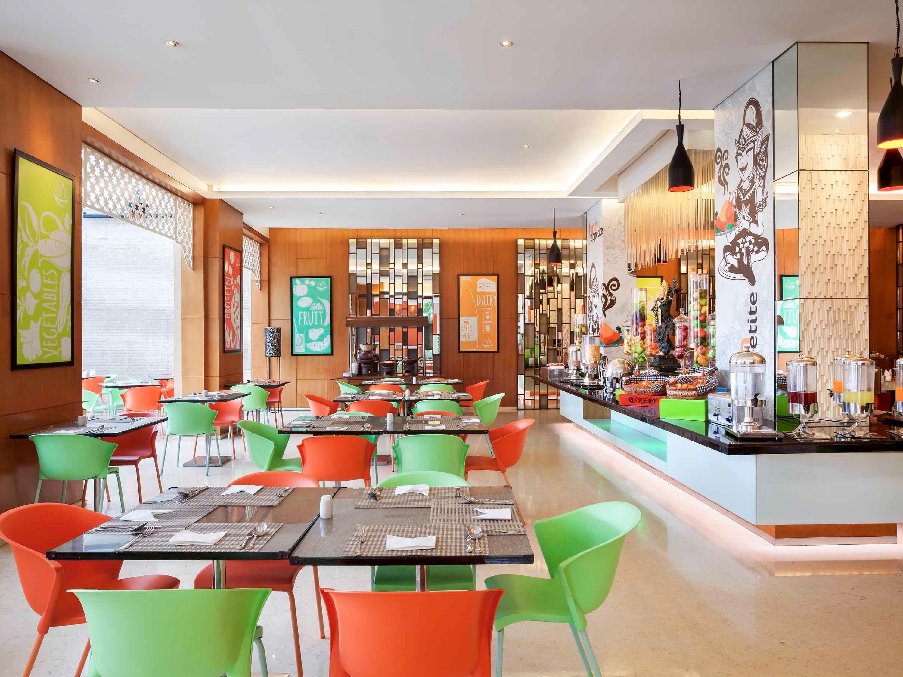 A modern restaurant with colorful chairs and tables, a bar area with various food and drink dispensers, and a wooden interior design.